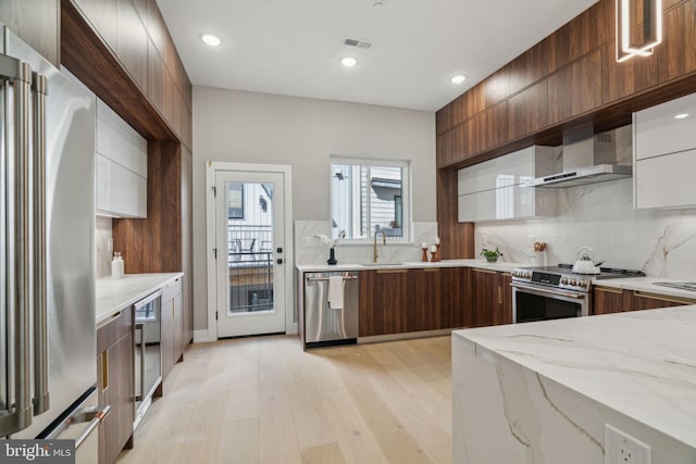 kitchen with visible vents, wall chimney exhaust hood, modern cabinets, appliances with stainless steel finishes, and light stone countertops