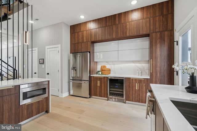 kitchen with appliances with stainless steel finishes, beverage cooler, light wood-style floors, and modern cabinets