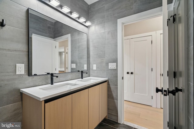 full bath with wood finished floors, double vanity, a sink, and tile walls