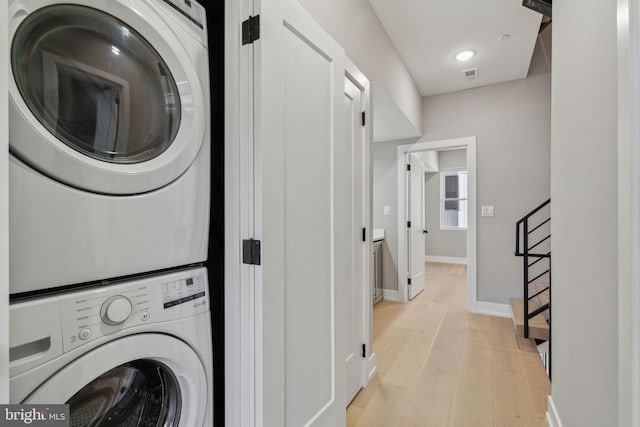 laundry area featuring laundry area, visible vents, light wood finished floors, baseboards, and stacked washer / drying machine