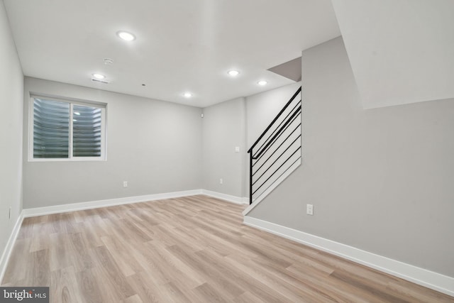 below grade area featuring light wood finished floors, baseboards, recessed lighting, and stairs