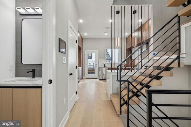 hallway with light wood-style floors, recessed lighting, a sink, and stairway
