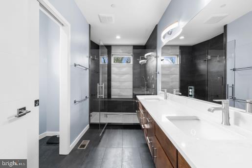 bathroom with double vanity, visible vents, a sink, and a stall shower