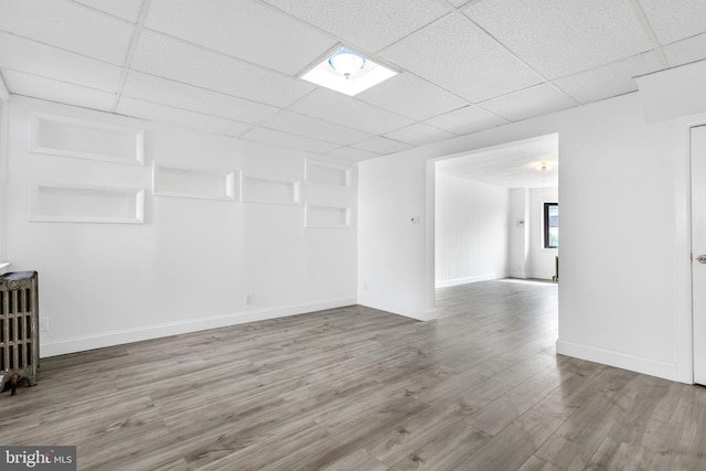 spare room with wood finished floors, radiator heating unit, baseboards, and a drop ceiling