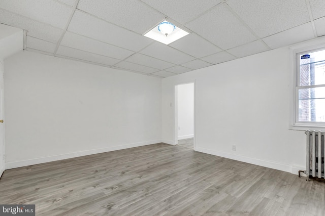 unfurnished room featuring a drop ceiling, baseboards, radiator, and wood finished floors