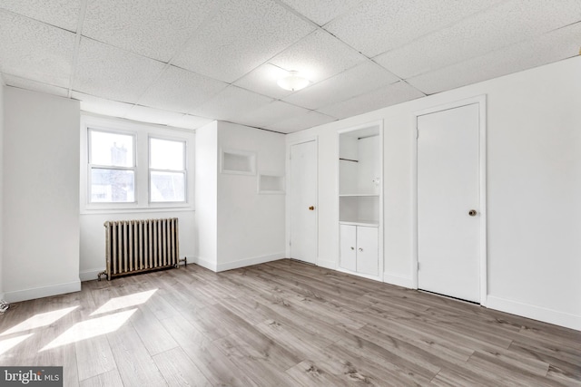 unfurnished room with radiator heating unit, a drop ceiling, baseboards, and wood finished floors