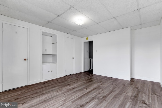 unfurnished bedroom featuring a paneled ceiling, baseboards, and wood finished floors