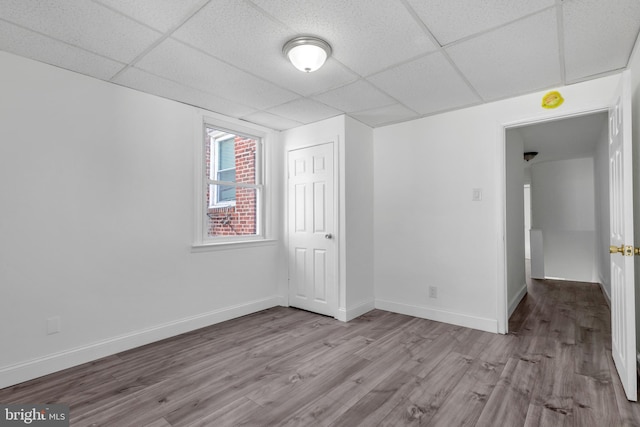 unfurnished room featuring wood finished floors, baseboards, and a drop ceiling