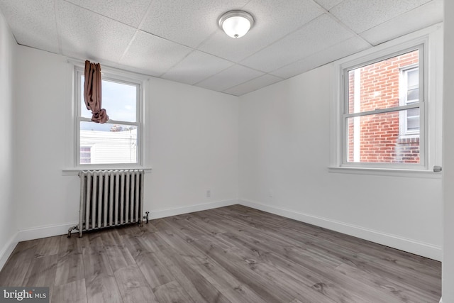 empty room with radiator heating unit, a paneled ceiling, baseboards, and wood finished floors