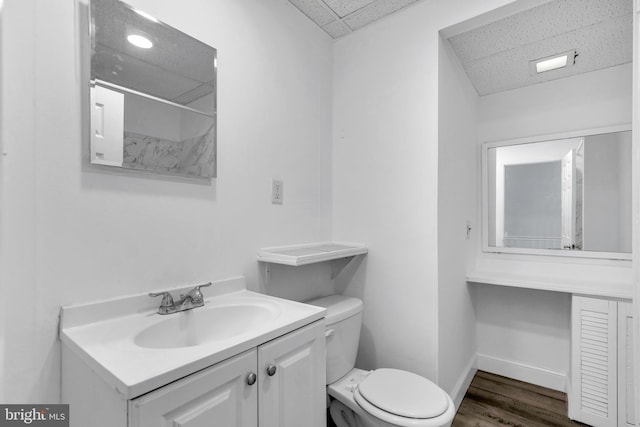 bathroom with toilet, wood finished floors, vanity, and baseboards