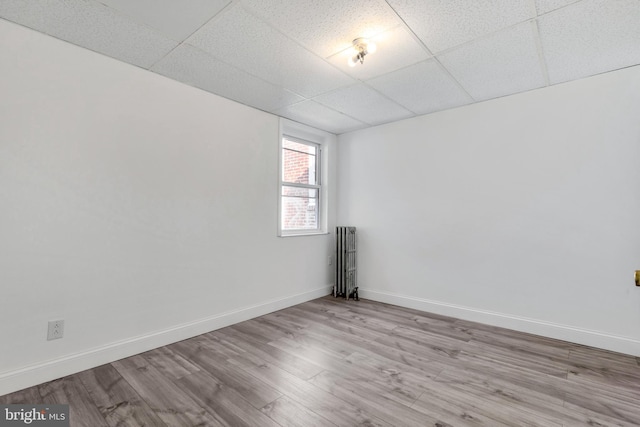 unfurnished room with radiator heating unit, a drop ceiling, wood finished floors, and baseboards