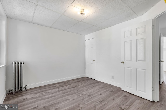 empty room with a paneled ceiling, radiator, wood finished floors, and baseboards