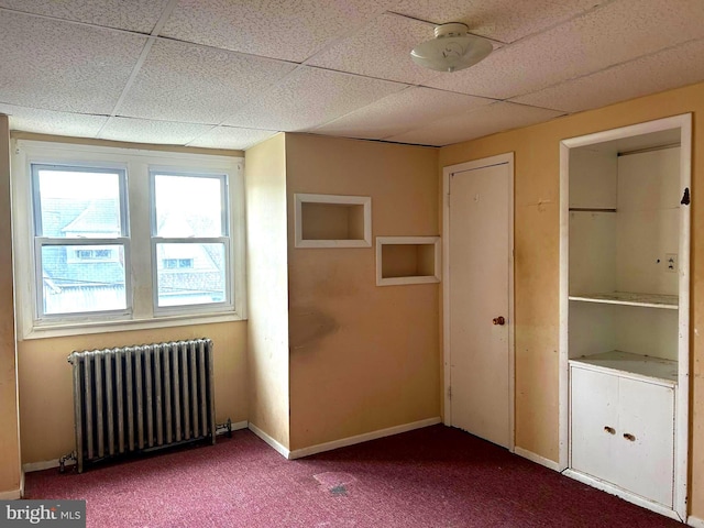 carpeted empty room with radiator heating unit, a drop ceiling, and baseboards