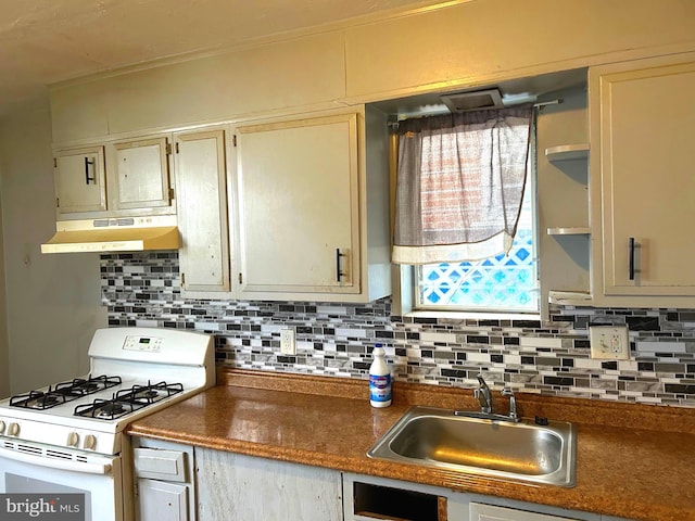 kitchen featuring white range with gas cooktop, under cabinet range hood, a sink, dark countertops, and backsplash