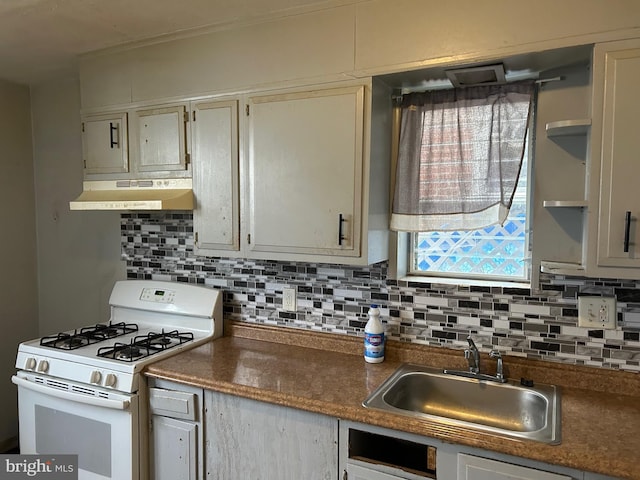 kitchen with tasteful backsplash, a sink, dark countertops, under cabinet range hood, and white gas range oven