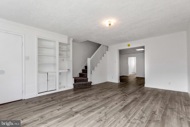 unfurnished living room with built in shelves, stairway, wood finished floors, and a textured ceiling