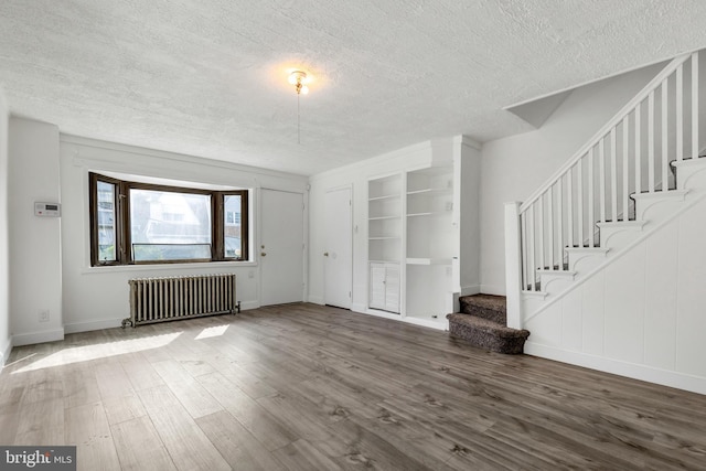 unfurnished living room with baseboards, a textured ceiling, radiator, wood finished floors, and stairs