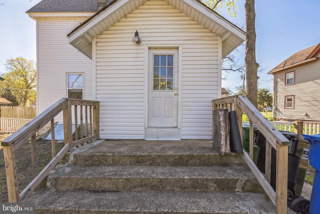 view of exterior entry featuring a shingled roof and fence