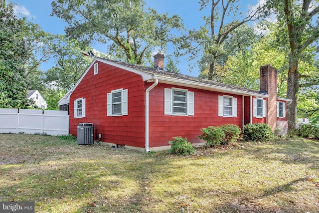 view of side of home with fence, cooling unit, a lawn, and a chimney