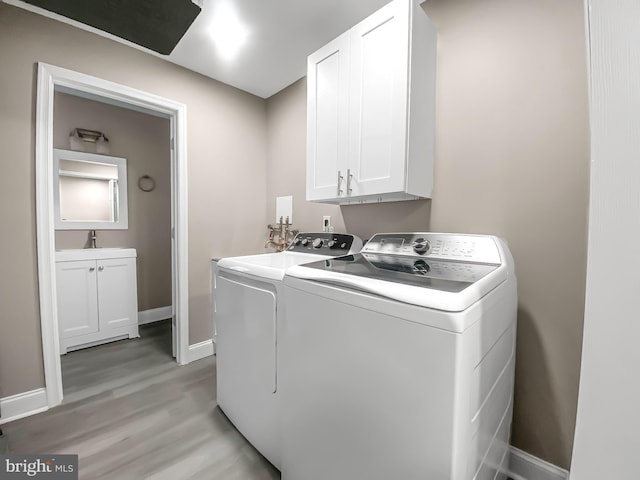 clothes washing area featuring baseboards, light wood-style floors, cabinet space, washer and dryer, and a sink