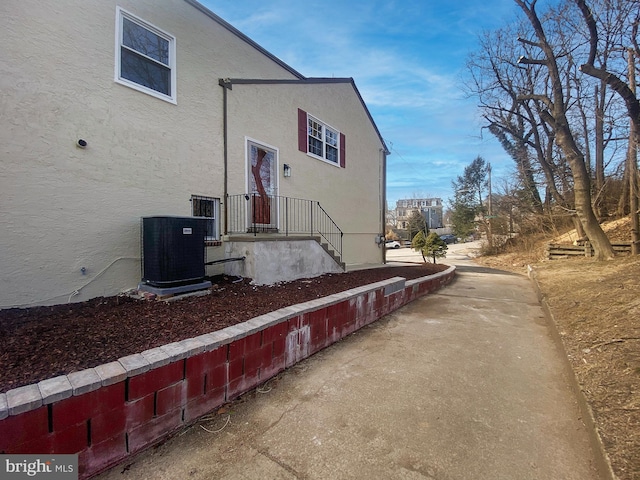 view of side of home with central AC unit and stucco siding