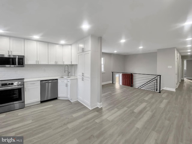 kitchen featuring a sink, light countertops, stainless steel appliances, open floor plan, and light wood finished floors