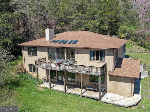 back of property with roof with shingles, a chimney, brick siding, a deck, and a lawn
