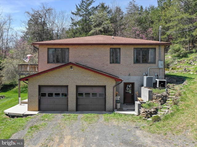 view of front of home with central air condition unit, an attached garage, driveway, and brick siding