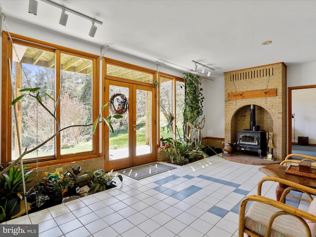 sunroom / solarium with rail lighting, a wood stove, french doors, and a healthy amount of sunlight