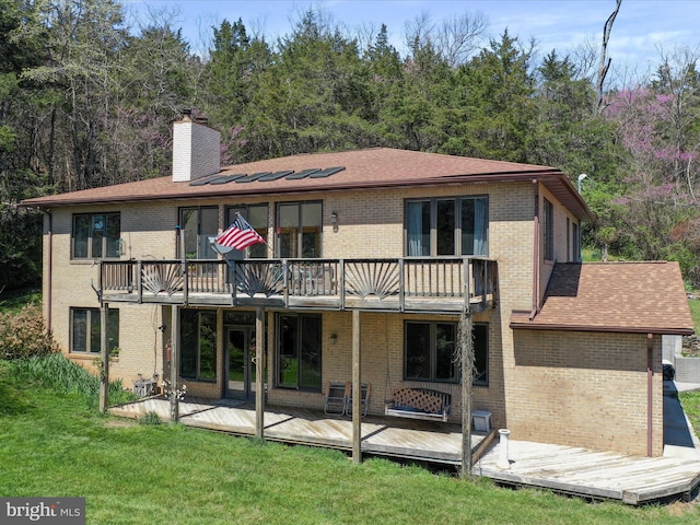 rear view of house featuring a yard, brick siding, a wooden deck, and a chimney