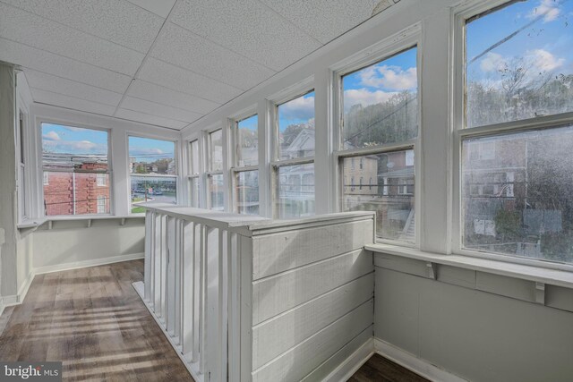unfurnished sunroom featuring wood finished floors, baseboards, and a paneled ceiling