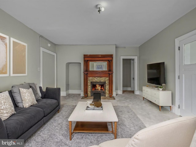 living area with light colored carpet, baseboards, and a stone fireplace