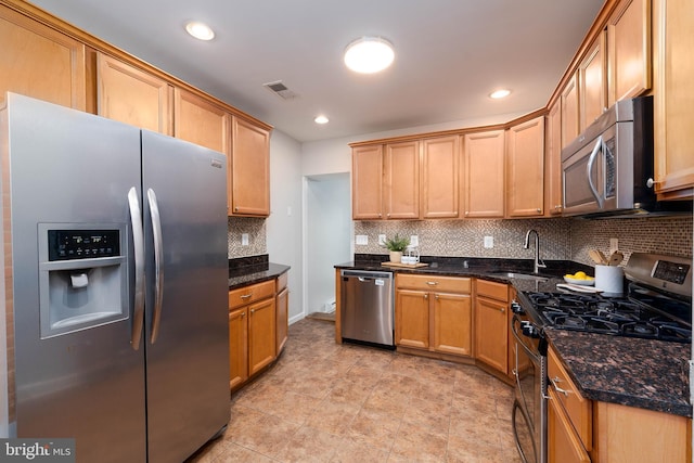 kitchen with stainless steel appliances, a sink, backsplash, dark stone countertops, and recessed lighting