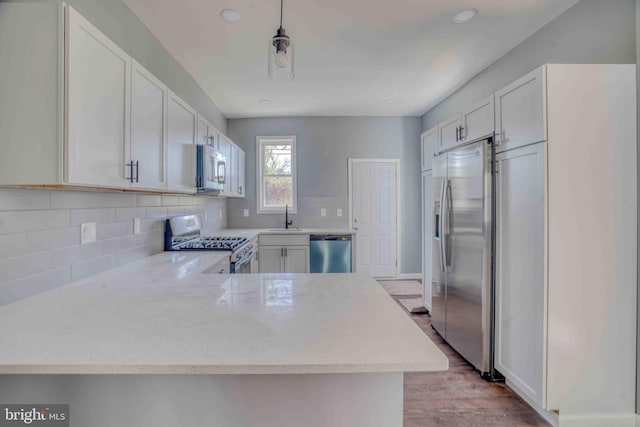 kitchen with tasteful backsplash, a sink, appliances with stainless steel finishes, a peninsula, and white cabinetry