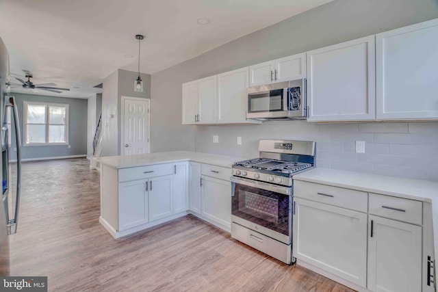 kitchen with a peninsula, light countertops, white cabinets, decorative backsplash, and appliances with stainless steel finishes