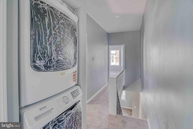 clothes washing area featuring stacked washer and dryer, baseboards, carpet, and laundry area