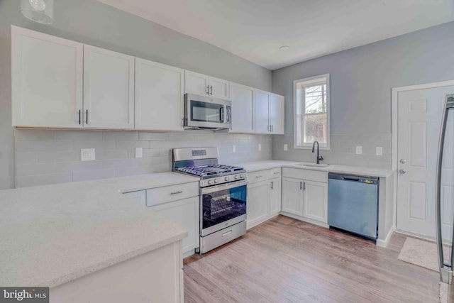 kitchen featuring white cabinets, light wood-style flooring, a sink, and appliances with stainless steel finishes