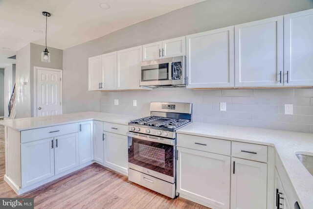 kitchen with light wood-style floors, a peninsula, white cabinetry, stainless steel appliances, and backsplash