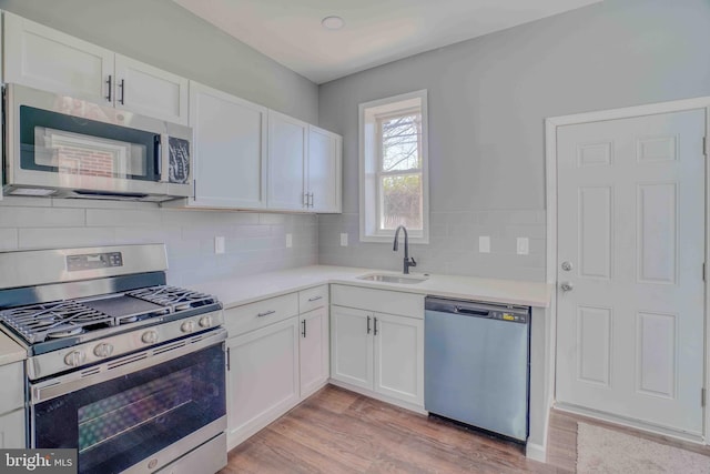 kitchen with appliances with stainless steel finishes, decorative backsplash, a sink, and white cabinetry