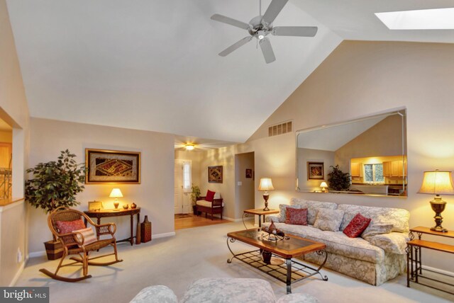 living room with a ceiling fan, carpet floors, visible vents, a skylight, and high vaulted ceiling