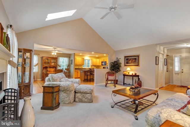 living room with light carpet, high vaulted ceiling, a ceiling fan, and a skylight