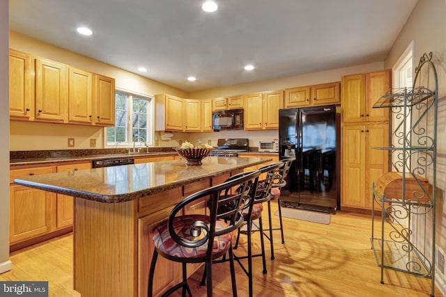 kitchen featuring light wood finished floors, light brown cabinetry, black appliances, and a breakfast bar