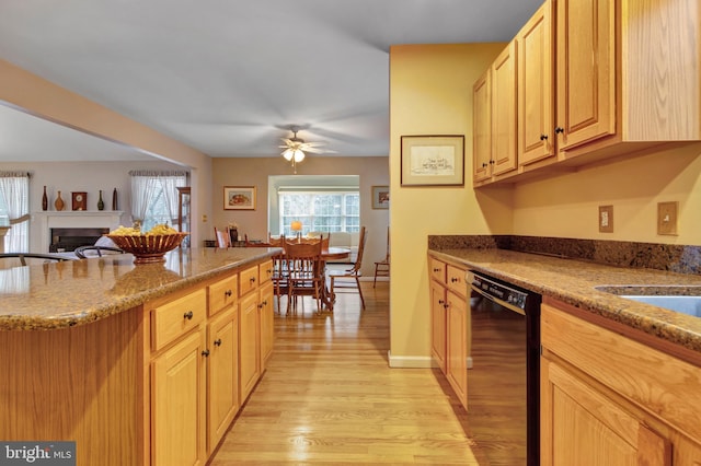 kitchen featuring black dishwasher, light wood-type flooring, a ceiling fan, a fireplace, and light stone counters