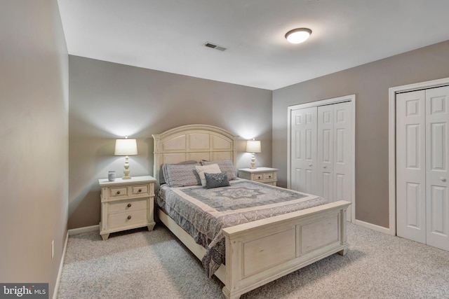 bedroom with visible vents, multiple closets, light carpet, and baseboards