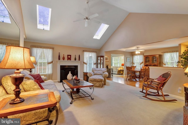living room with ceiling fan, a fireplace, a skylight, high vaulted ceiling, and carpet flooring