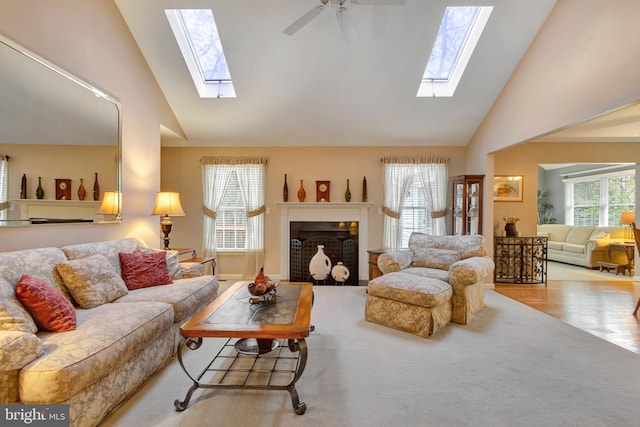 living area with wood finished floors, high vaulted ceiling, a ceiling fan, and a skylight