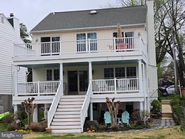 rear view of house with a porch, a shingled roof, stairs, and a chimney