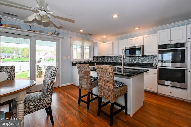 kitchen with crown molding, white cabinets, a kitchen bar, decorative backsplash, and stainless steel appliances