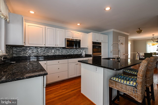kitchen featuring crown molding, a breakfast bar, stainless steel microwave, a sink, and decorative backsplash