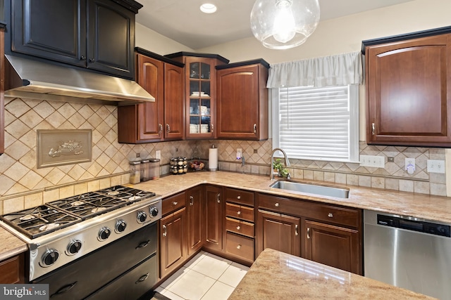 kitchen featuring light stone counters, under cabinet range hood, stainless steel appliances, a sink, and glass insert cabinets